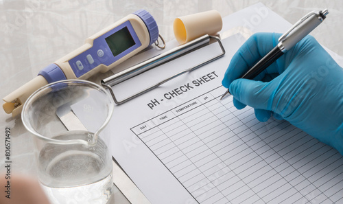 hand with glove writing on a ph check sheet. Checking the ph of the water