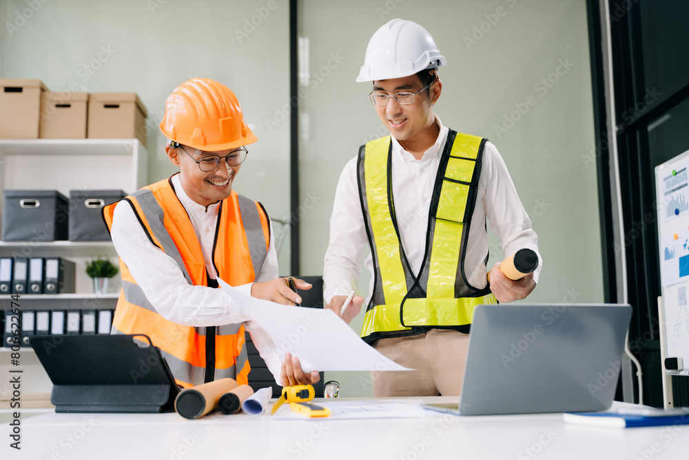 Contractor and architect looking at plan, tablet, laptop and talking about working on big project. Contractor and architect looking at plan, tablet, laptop and talking about working on big project.