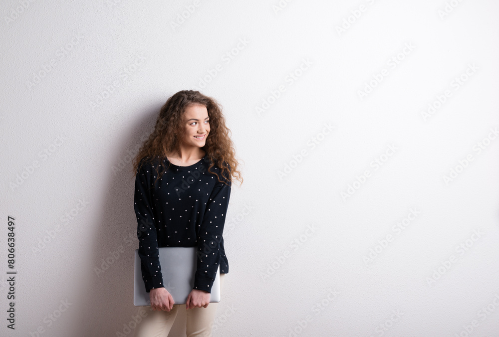 Portrait of a gorgeous teenage girl with curly hair, holding notebook, leaning against wall. Studio shot, white background with copy space Portrait of a gorgeous teenage girl with curly hair, holding notebook, leaning against wall. Studio shot, white background with copy space
