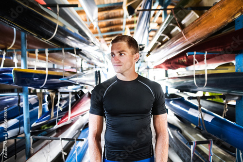 Portrat of young canoeist standing in the middle of stacked canoes. Concept of canoeing as dynamic and adventurous sport. photo