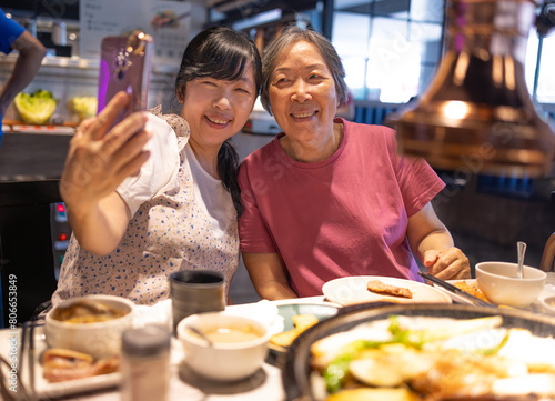 Happy mother and daughter celebrating mothers day and taking selfie at restaurant