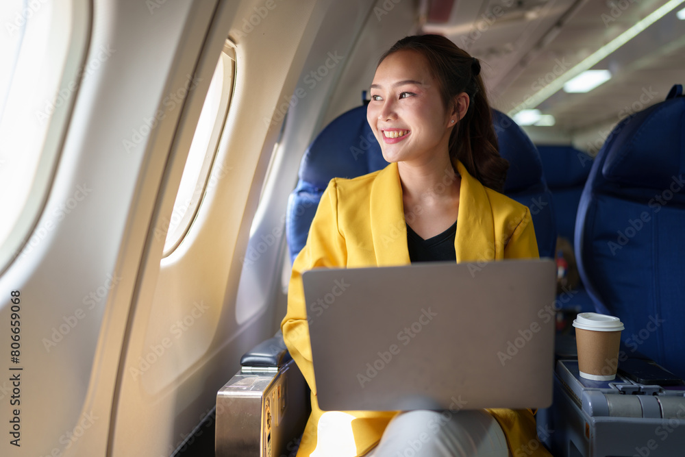 Confident businesswoman in formal clothes looking out of airplane window during flight while working on laptop computer Online internet connection, travel concept, business tourism. Confident businesswoman in formal clothes looking out of airplane window during flight while working on laptop computer Online internet connection, travel concept, business tourism.