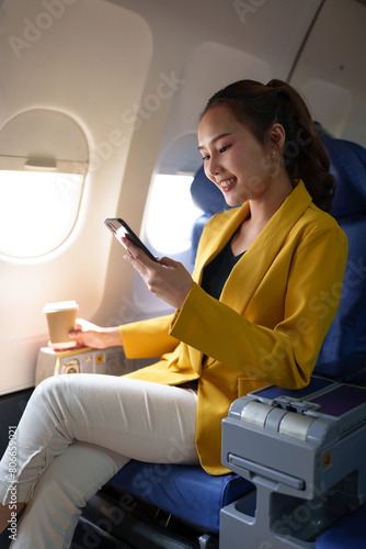 Young woman  business woman in a yellow suit is using a smartphone to communicate with customers and Friends on plane and laptop with Wi-Fi internet connection on plane. Travel concept.