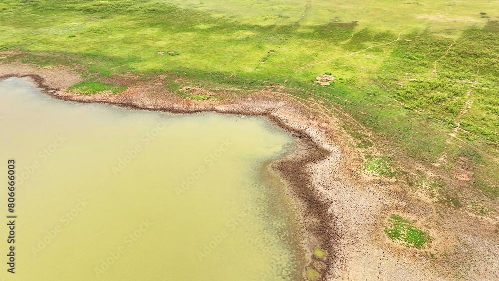 Aerial vista reveals parched earth and sparse vegetation in a drought-stricken dam, showcasing the stark impact of receding water levels, emblematic of nature's struggle under severe drought.
