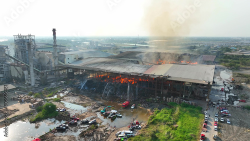 A scene of chaos unfolds at the industrial facility, marked by intense fire damage. Collapsed roofs and fierce flames engulf the site, shrouding it in smoke, signaling a significant disaster.
 photo
