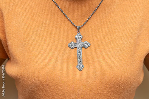 Silver vintage crucifix pendant or cross sign and chain necklace and close-up orange sweater. Easter festival. Faith. Christian. Jesus