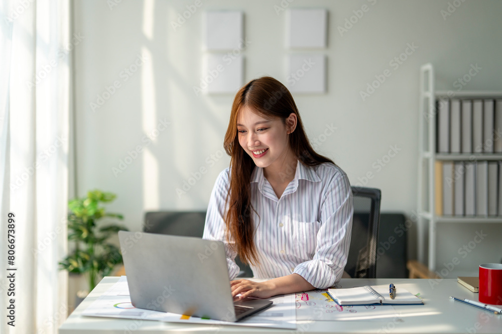 A woman is sitting at a desk with a laptop in front of her. She is smiling and she is enjoying her work