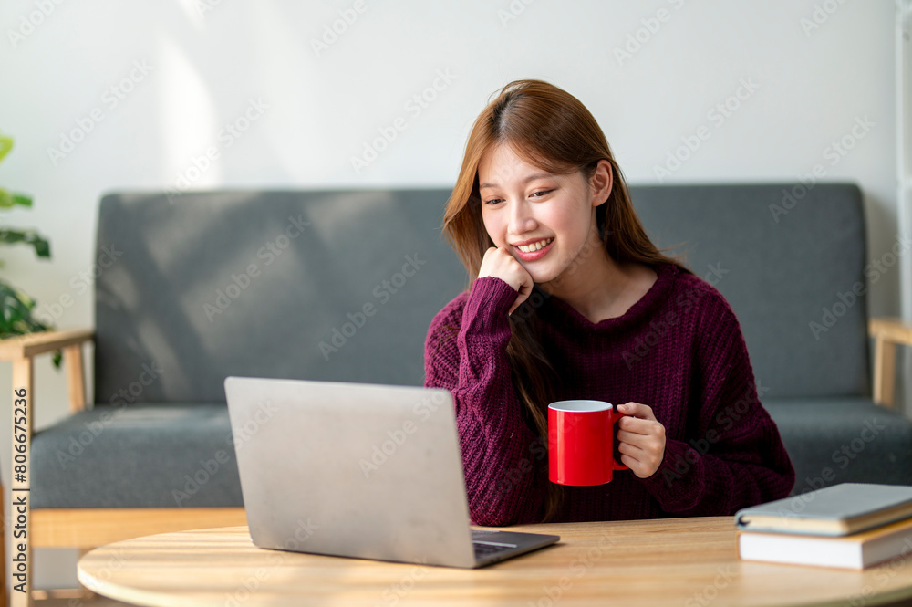 A woman is sitting on a couch with a laptop and a red coffee mug in front of her. She is smiling and she is enjoying her time A woman is sitting on a couch with a laptop and a red coffee mug in front of her. She is smiling and she is enjoying her time