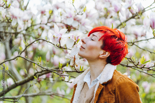 Beautiful redhead woman eyes closed smelling magnolia blossom in park photo