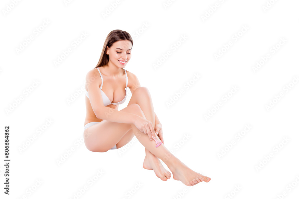 Obraz premium Portrait of pretty woman shaving slim long legs carefully sitting over white background