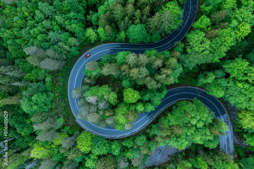 Germany, Bavaria, Aerial view of car driving along asphalt road winding through green forest in Bavarian Alps