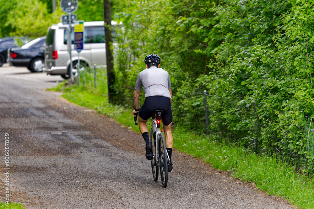 Male cyclist with pigtail on racing bicycle surrounded by bushes on a rural road at Swiss City of Zürich on a spring day. Photo taken May 5th, 2024, Zurich, Switzerland. Male cyclist with pigtail on racing bicycle surrounded by bushes on a rural road at Swiss City of Zürich on a spring day. Photo taken May 5th, 2024, Zurich, Switzerland.