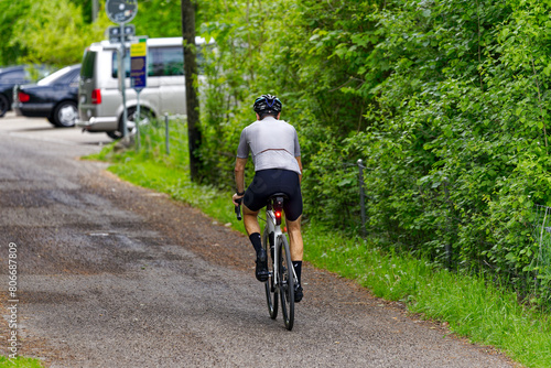 Male cyclist with pigtail on racing bicycle surrounded by bushes on a rural road at Swiss City of Zürich on a spring day. Photo taken May 5th, 2024, Zurich, Switzerland.