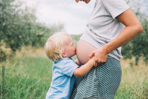 Child boy kissing belly of pregnant her mother on nature background. photo