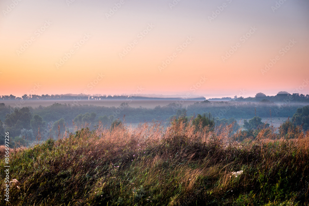 Red sunrise over the field with trees and forest . Morning at summer . Fog over the field and trees . Beautiful landsapes . Red sky and blue hour on nature . Smoothly foggy morning 