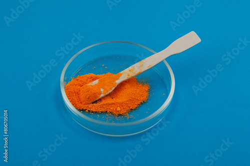 Tartrazine powder in Petri dish on blue background. Food coloring, pigment. Food additive E102. Tartrazine is a synthetic lemon yellow azo dye. CI 19140 or FD&C