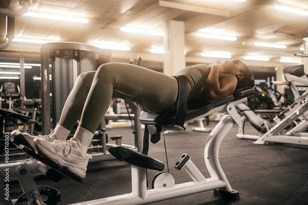 A muscular black sportswoman is practicing hip thrusts on a gym machine.