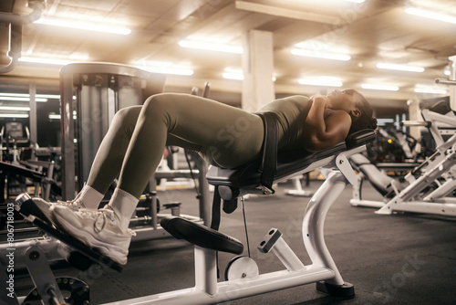 A muscular black sportswoman is practicing hip thrusts on a gym machine.