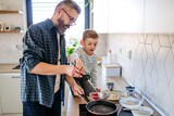 Boy helping father to make pancake. Father spending time with son at home, making snack together, cooking. Fathers day concept.