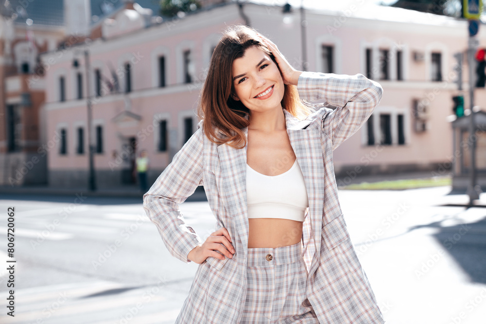 Portrait of young beautiful brunette woman wearing nice trendy plaid suit jacket. Sexy smiling model posing in the street at sunny day. Fashionable female outdoors. Cheerful and happy