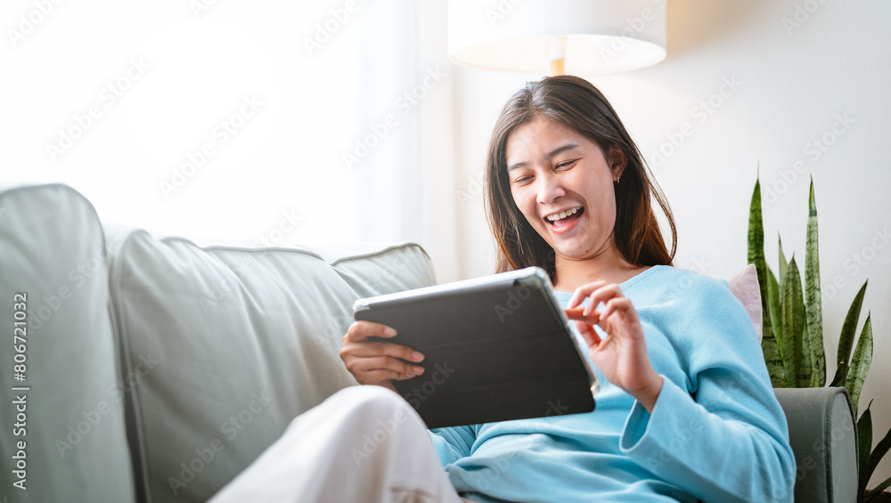 sofa, pretty, couch, relax, lying, reading, social, smile, person, room. A woman is sitting on a couch and smiling while holding a tablet. She is enjoying her time on the device. sofa, pretty, couch, relax, lying, reading, social, smile, person, room. A woman is sitting on a couch and smiling while holding a tablet. She is enjoying her time on the device.
