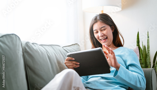 sofa, pretty, couch, relax, lying, reading, social, smile, person, room. A woman is sitting on a couch and smiling while holding a tablet. She is enjoying her time on the device.