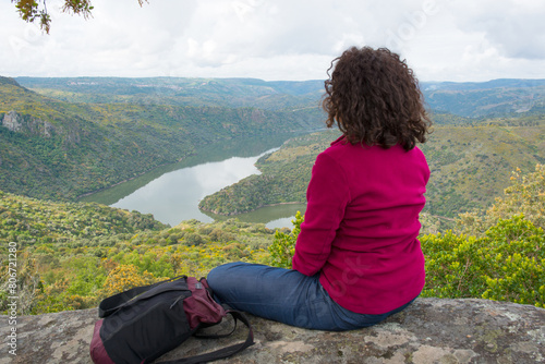 Rear view of woman sitting on mountain looking to beatiful landscape with river photo