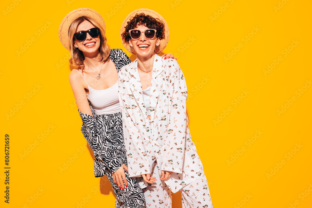 Obraz premium Two young beautiful smiling brunette hipster female in trendy summer costume clothes. Sexy women posing near yellow wall in studio. Positive models having fun. Cheerful and happy. In hat, sunglasses