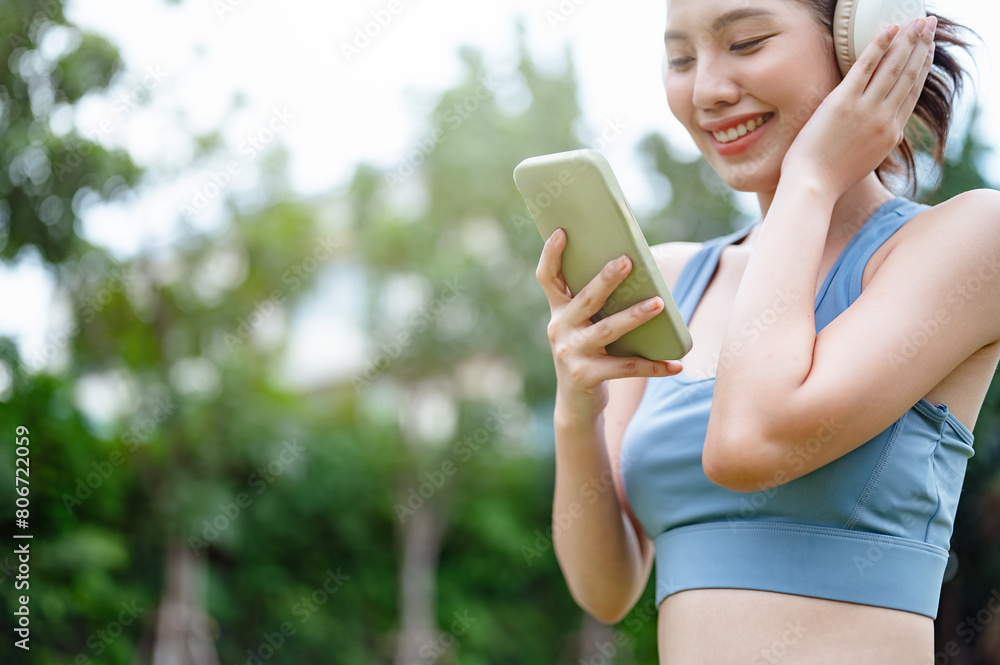 training, fit, fitness, exercise, run, runner, sports, women, jogging, jogger. A woman is smiling while holding a cell phone. She is wearing headphones and she is listening to music. training, fit, fitness, exercise, run, runner, sports, women, jogging, jogger. A woman is smiling while holding a cell phone. She is wearing headphones and she is listening to music.
