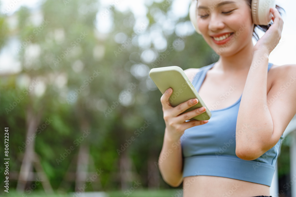 sporty, fitness, exercise, run, runner, sports, jogging, training, jogger, health. A woman is smiling while holding a cell phone. She is wearing headphones and she is listening to music.