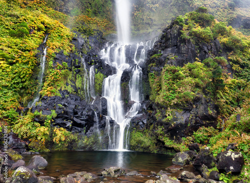 The Po  o do Bacalhau waterfall in the Flores island of Azores. Green hills and fields. Sunny weather.