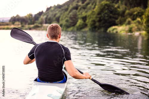 Canoeist man sitting in canoe holding paddle, in water. Concept of canoeing as dynamic and adventurous sport. Rear view, sportman looking at water surface, paddling photo