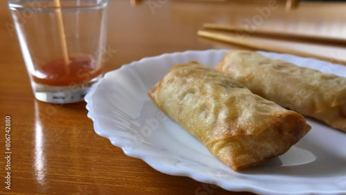 Chinese spring rolls with red sweet and sour sauce, Chinese chopsticks. Asian Chinese cuisine. background with brown table.