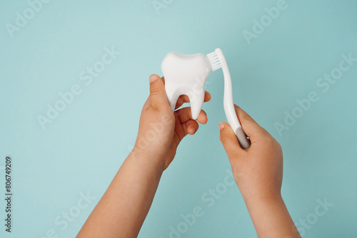 Child's hands holding white tooth and toothbrush on blue background. Healthy care teeth concept