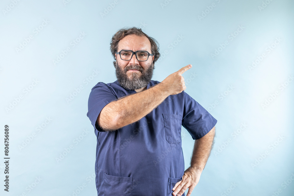 Fototapeta premium Horizontal banner of smiling young male doctor showing and presenting something with hand, isolated on blue background with copy space on right