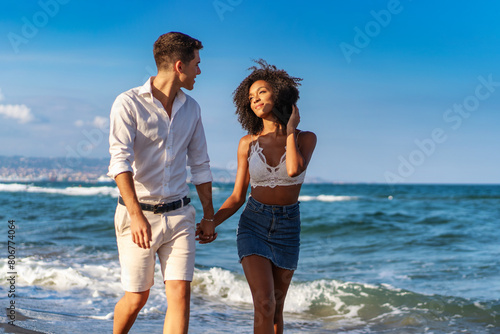 Young interracial couple - walking hand in hand on a sandy beach, enjoying a romantic and joyful stroll together - warm, vibrant. (ID: 806774064)