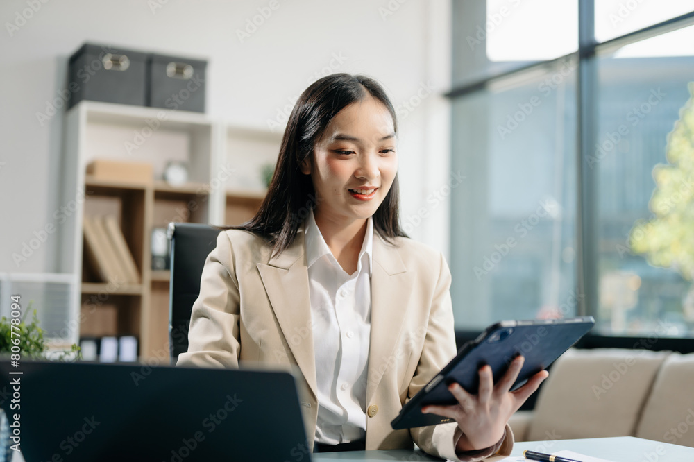 Asian woman using laptop and tablet while sitting at her working place. Concentrated at work. Asian woman using laptop and tablet while sitting at her working place. Concentrated at work.