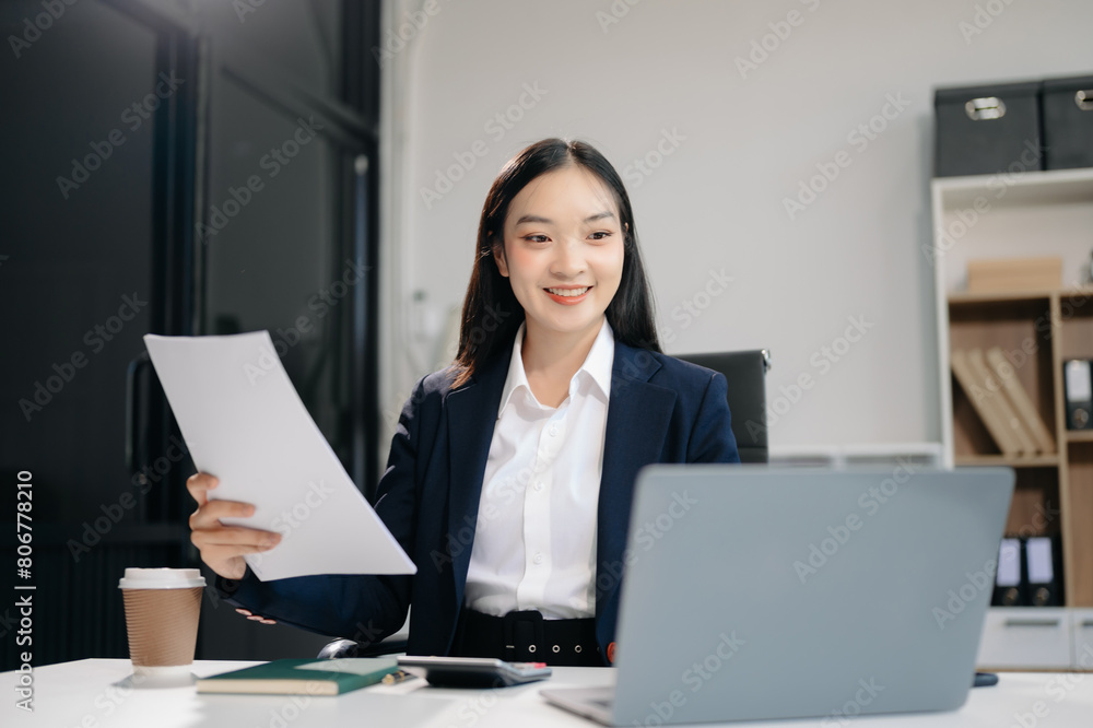 Asian woman using laptop and tablet while sitting at her working place. Concentrated at work. Asian woman using laptop and tablet while sitting at her working place. Concentrated at work.