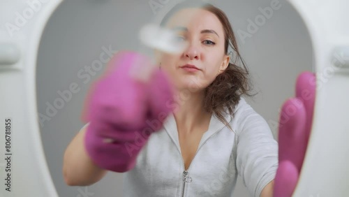Woman cleans toilet with brush. Woman dressed in white shirt and pink gloves at toilet restroom for cleaning or organizing. Female cleaner housekeeper housewife. View from toilet bottom. Cleanliness photo