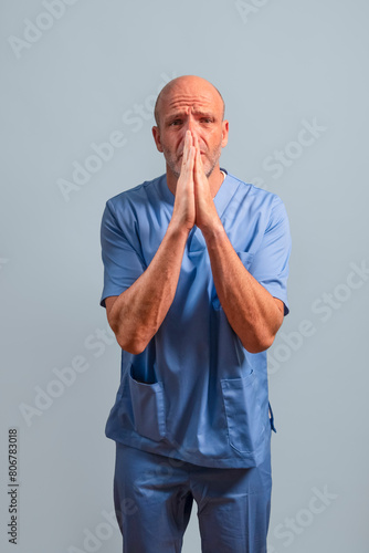 Portrait of a physiotherapist in light blue gown and hands together pleading.