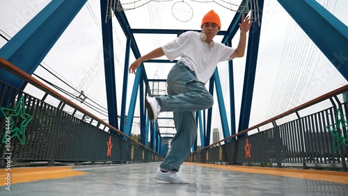 Professional break dancer perform street dance footstep at bridge. Asian hipster wear headphone while doing freeze pose. Break dancer, street dancer freestyle concept. Outdoor sport 2024. Sprightly.