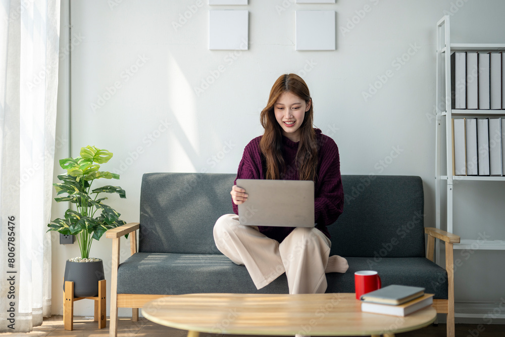 A woman is sitting on a couch with a laptop in front of her. She is smiling and she is enjoying her time. The room has a cozy and comfortable atmosphere, with a potted plant A woman is sitting on a couch with a laptop in front of her. She is smiling and she is enjoying her time. The room has a cozy and comfortable atmosphere, with a potted plant