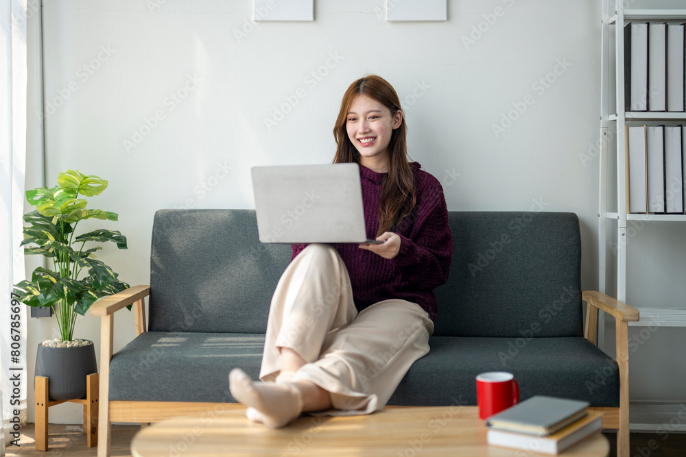 A woman is sitting on a couch with a laptop in her lap. She is smiling and she is enjoying her time. The room has a cozy and comfortable atmosphere, with a potted plant and a cup nearby A woman is sitting on a couch with a laptop in her lap. She is smiling and she is enjoying her time. The room has a cozy and comfortable atmosphere, with a potted plant and a cup nearby