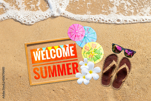Welcome summer sign with colourful paper umbrella and summer fashion on sandy beach, outdoor day light