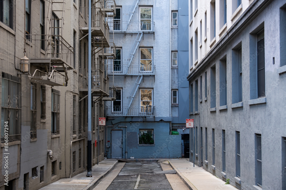 Fototapeta premium Backyard in downtown San Francisco (USA). Facades, balconies, windows, floor and walls of city houses in shades of grey, white and pale blue. Dead end small road with vanishing point perspective.