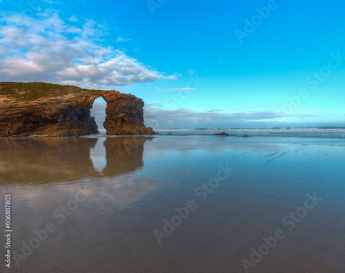 The stone arch of As Catedrais beach is reflected in the waters of low tide photo