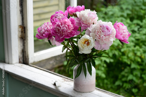 A bouquet of pink peonies in a vase on the windowsill of an old country home, a summer cottage.