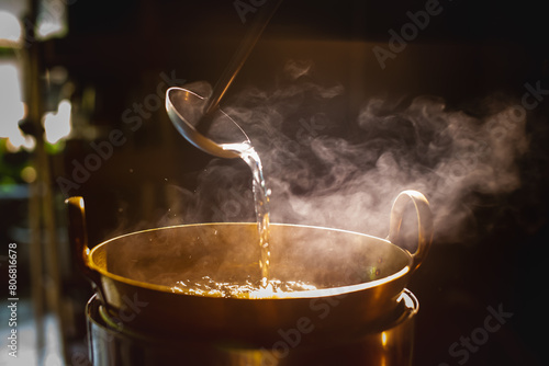 A brass pot is steaming while the chef cooks desserts using a ladle to stir in the brass pot.