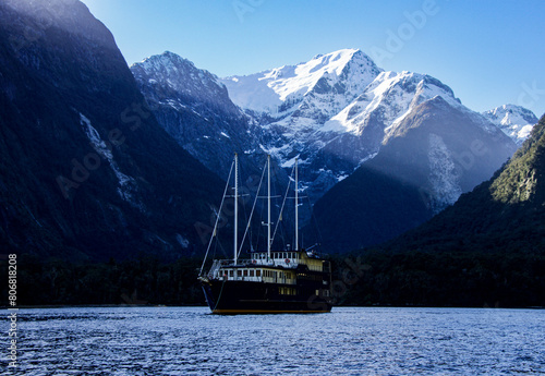 Boat on Milford Sound Fiordland New Zealand surrounded by snow clapped mountains with sun rays shining  photo