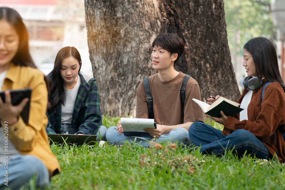 Asian college student focusing on laptop work or reading while other classmates in the background, outdoor portrait on campus. Asian college student focusing on laptop work or reading while other classmates in the background, outdoor portrait on campus.